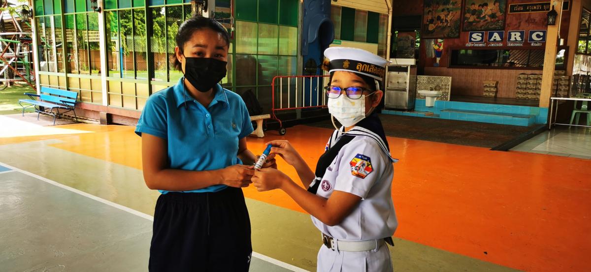 จิตอาสาแจกสเปรย์ แอลกอฮอล์สำหรับผู้ปกครองที่เข้ามาติดต่อภายในโรงเรียน