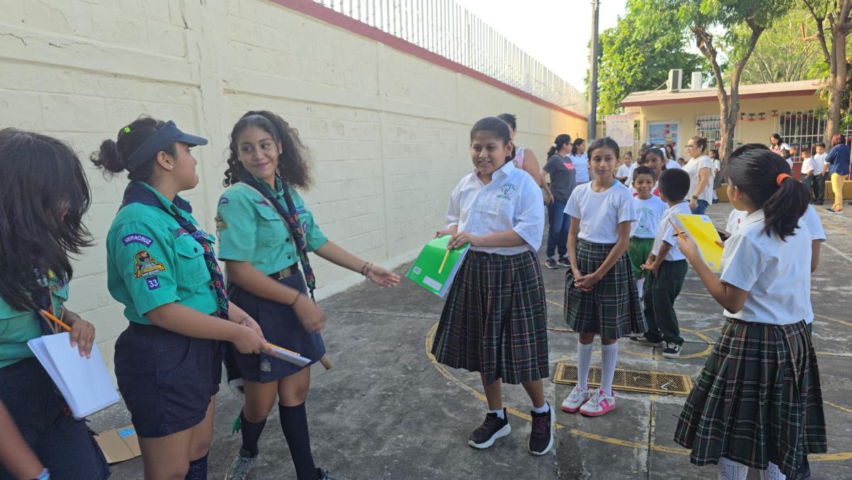 Tres scouts entregando libretas y lápices a los niños beneficiarios del proyecto