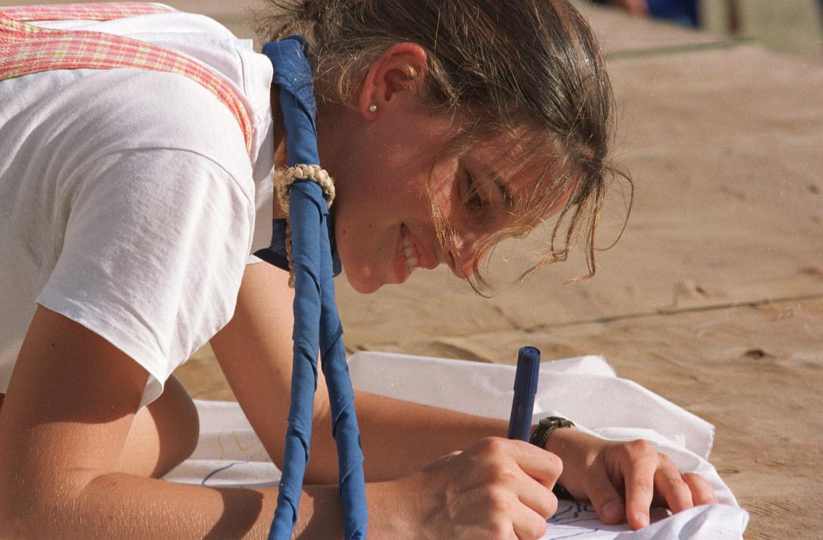A young scout writing on a paper on the ground