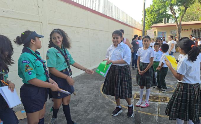 Tres scouts entregando libretas y lápices a los niños beneficiarios del proyecto